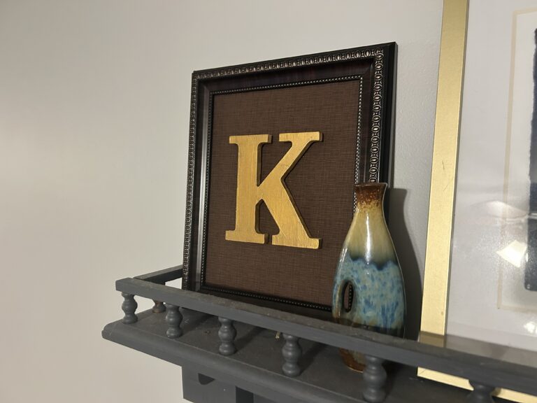 A brown frame with brown fabric and a gold K initial in the center